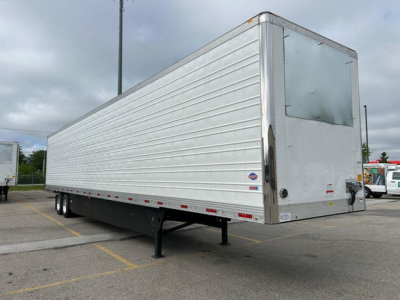 Utility refrigerated trailer on a parking lot showing side paneling, rear doors, and front hitch. Trailer is aluminum with ribbed sides and a raised refrigerated cap.