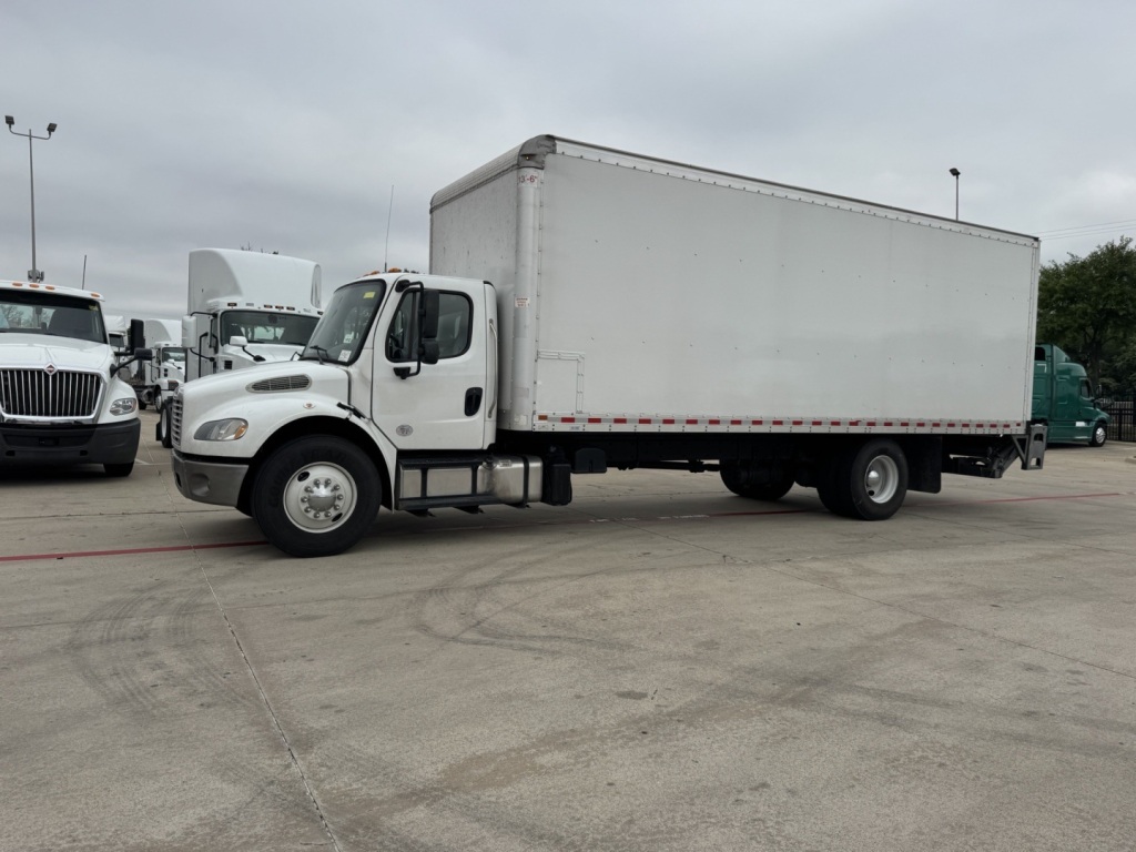 Freightliner M2 medium-duty truck with a box body, side view showing cab and cargo trailer in a dealership lot.
