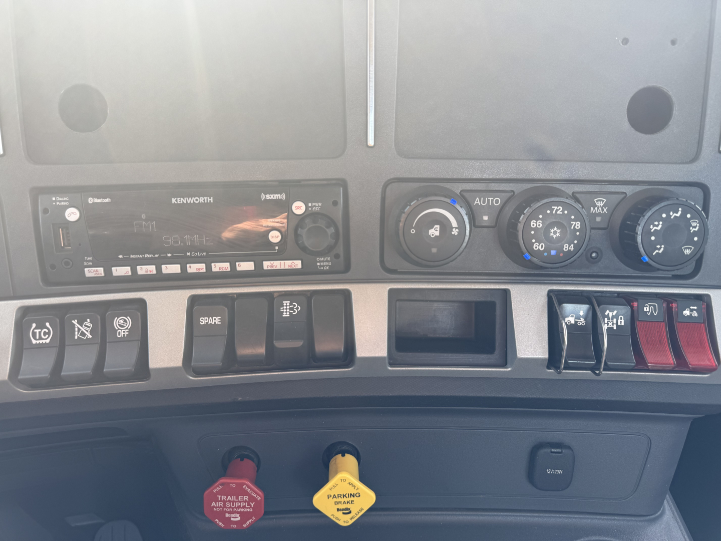 Kenworth T680 dashboard with climate controls, radio, switches, and warning labels visible; dashboard center area shows ignition and various gauges.