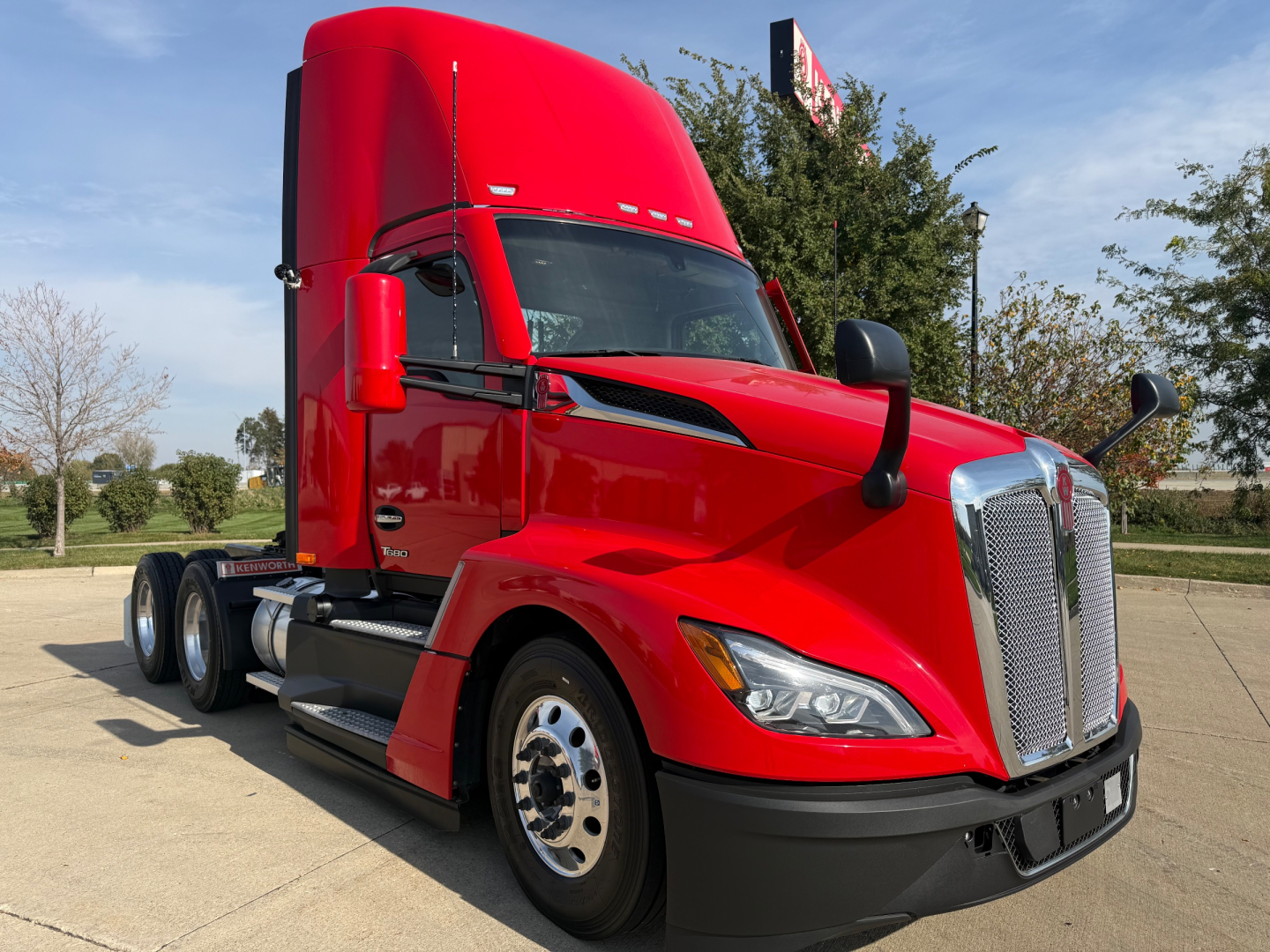 Kenworth T680 daycab tractor in red, front three-quarter view with sleeperless cab, large chrome grille, dual rear axles, Excel aluminum wheels, side mirrors.