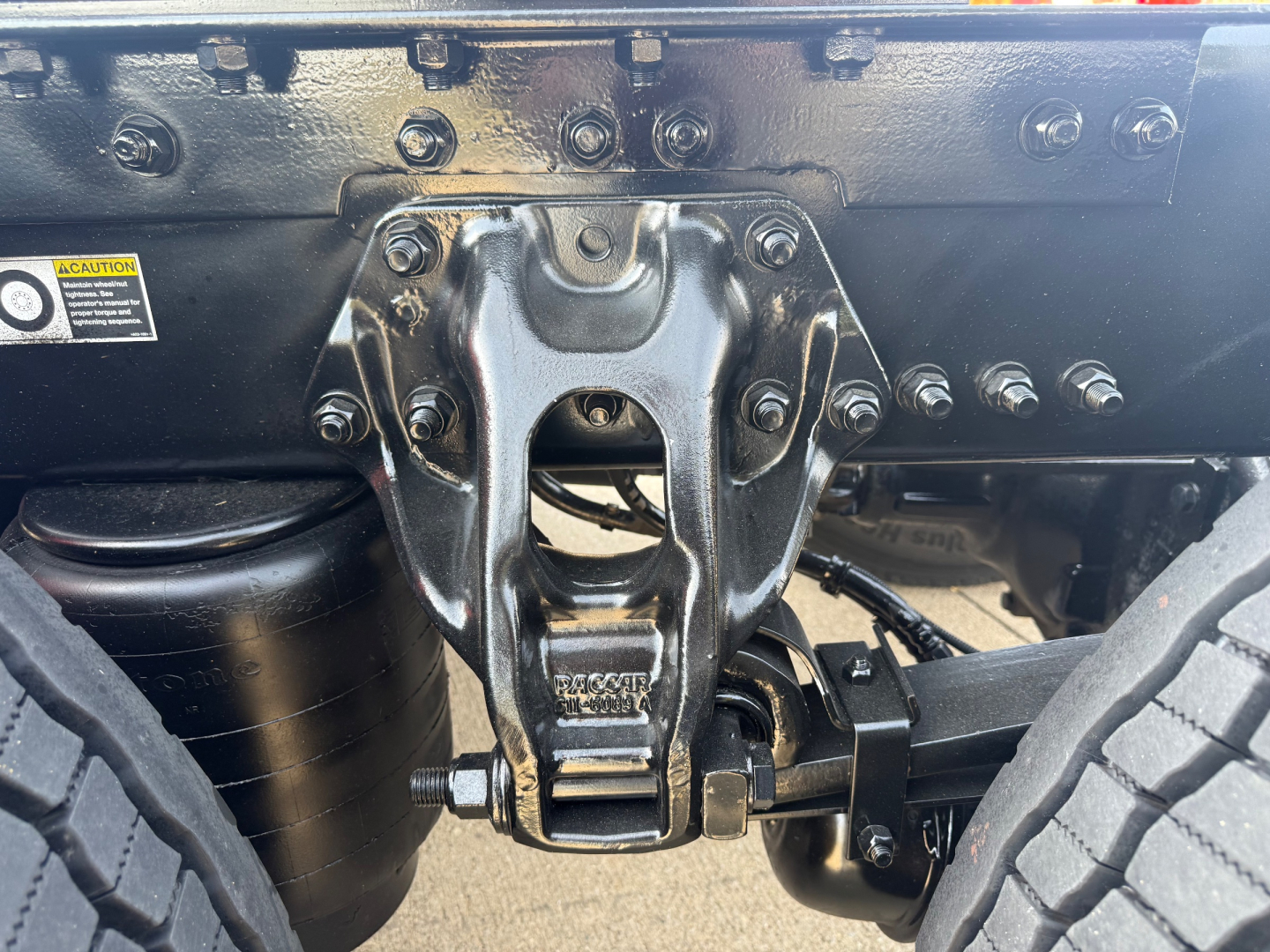 Kenworth truck undercarriage showing front suspension link and bolt assembly with bolts and frame braces.