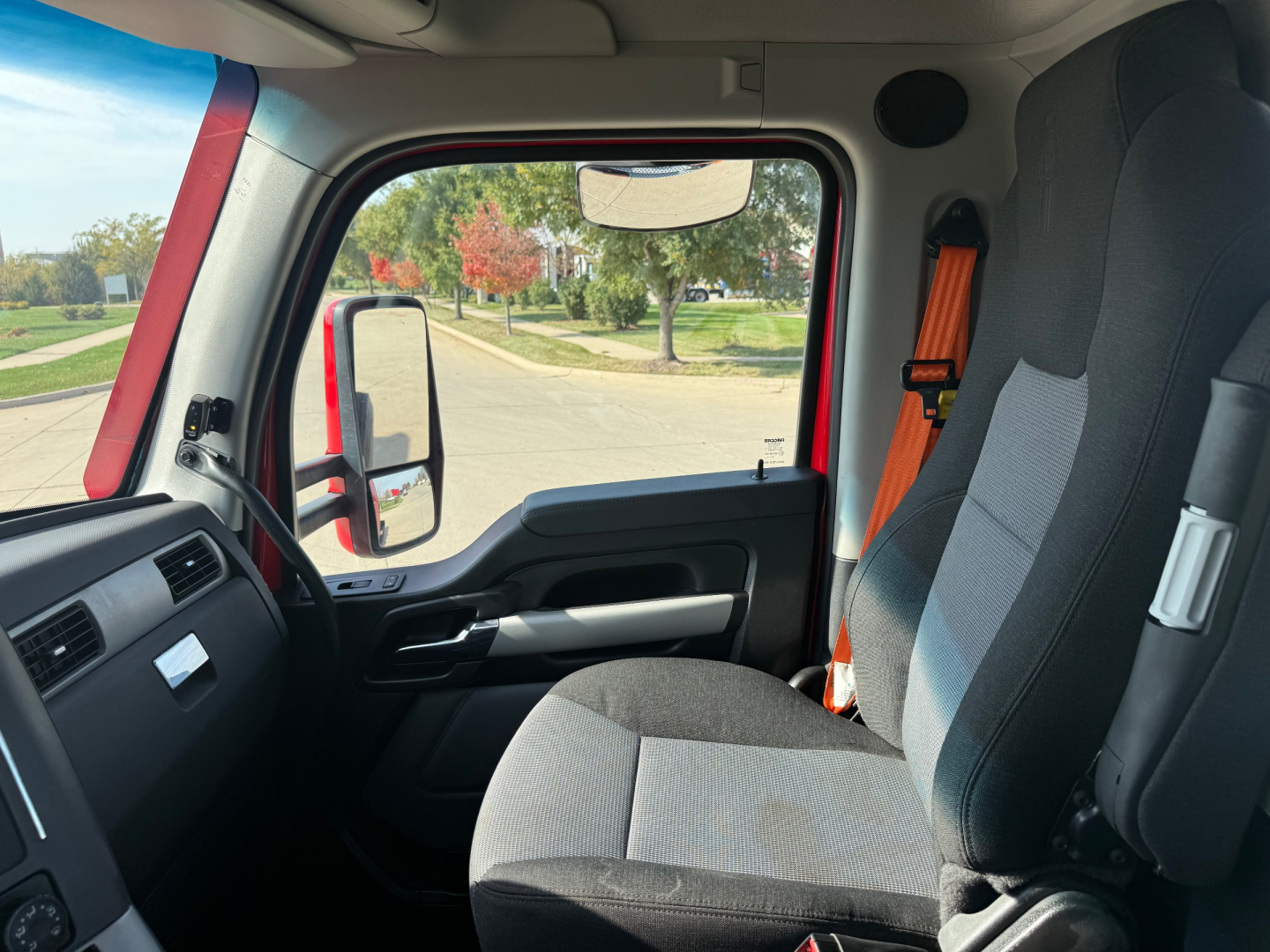 Kenworth T680 truck interior cab view showing driver seat, door panel, window, seat belt, and part of dashboard.