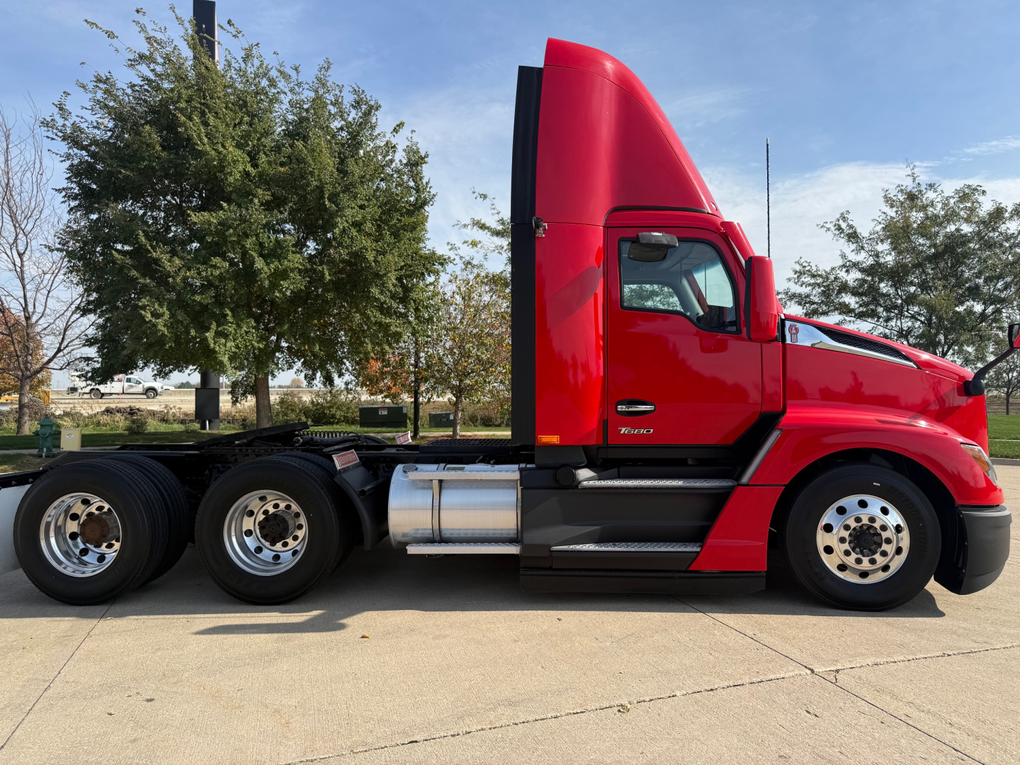 Kenworth T680 daytime cab tractor in red, side profile view showing fuel tanks and rear axles.