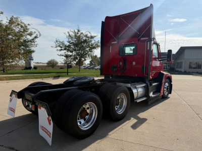Kenworth T680 conventional daycab tractor in red, rear view showing dual rear axles and fifth wheel, sleeper cab with sun visor, side mirrors, and mud flaps.