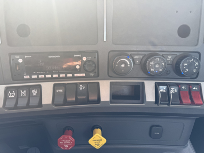 Kenworth T680 dashboard with climate controls, radio, switches, and warning labels visible; dashboard center area shows ignition and various gauges.
