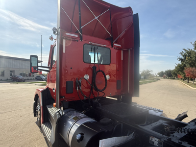 Kenworth T680 sleeper cab rear view with red cab, exposed air lines, and fifth wheel area in a truck yard.
