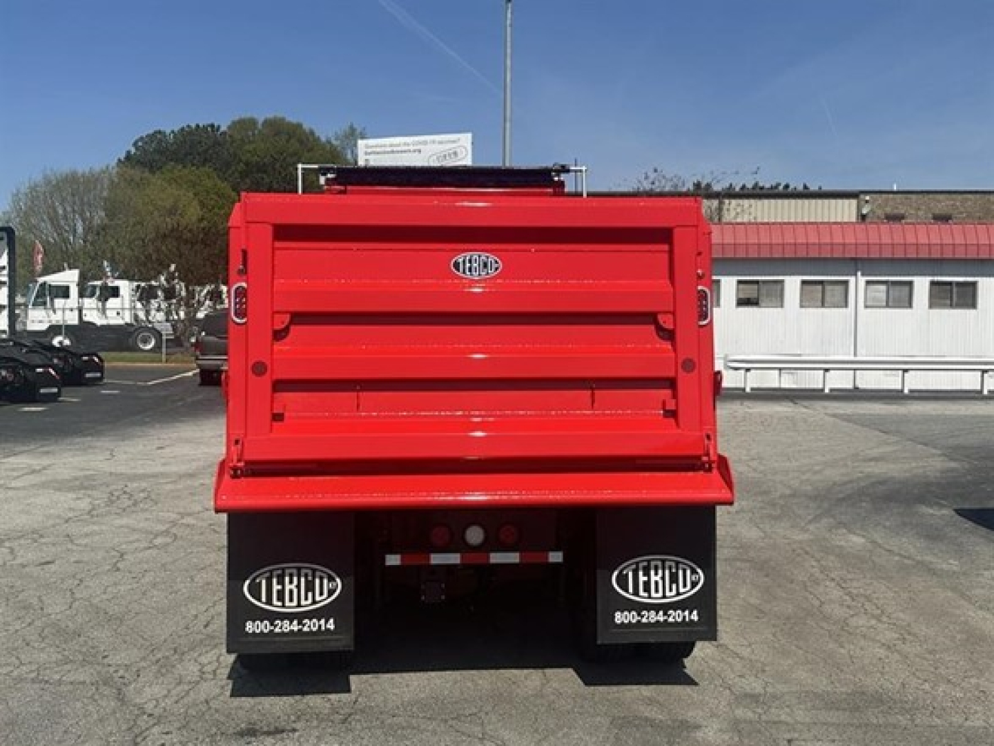 Rear view of a bright red Western Star dump body with black mudflaps displaying EBCC logos; license-plate area shows rear bumper and reflective markings.