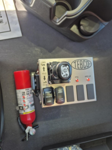 Truck control panel with TEBCD label and multiple switches, throttle dial, and a red fire extinguisher visible.