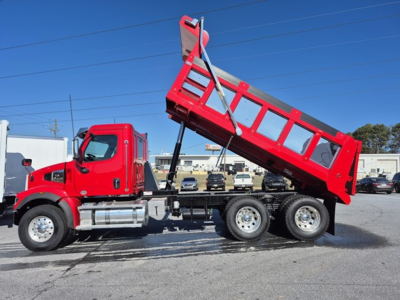 Red Western Star 47x dump truck with tilted bed in a dealership lot, showing axles and dump bed mechanism.