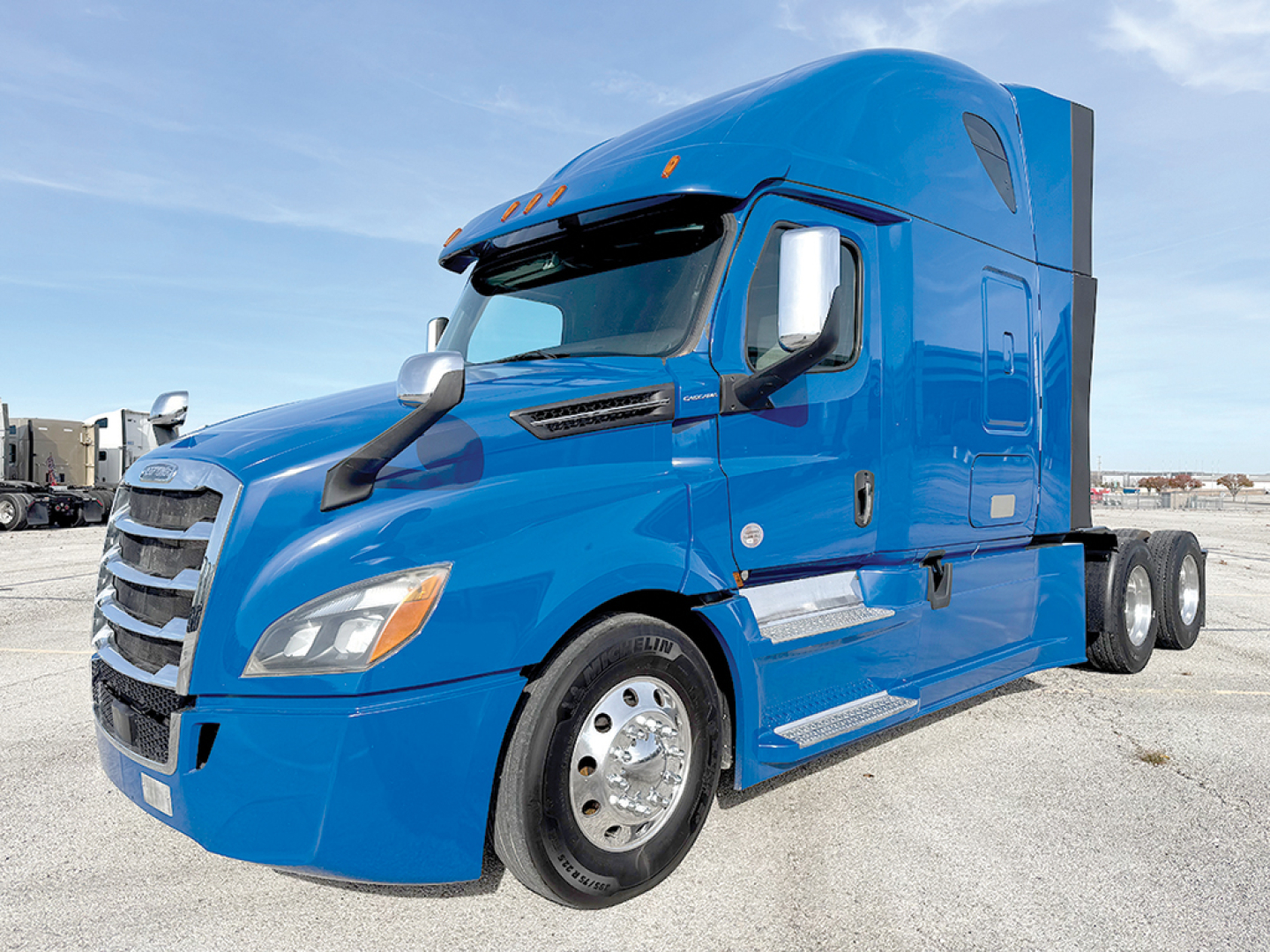 Blue Freightliner Cascadia126 truck cab close-up showing side mirror, front grille, and wheel.