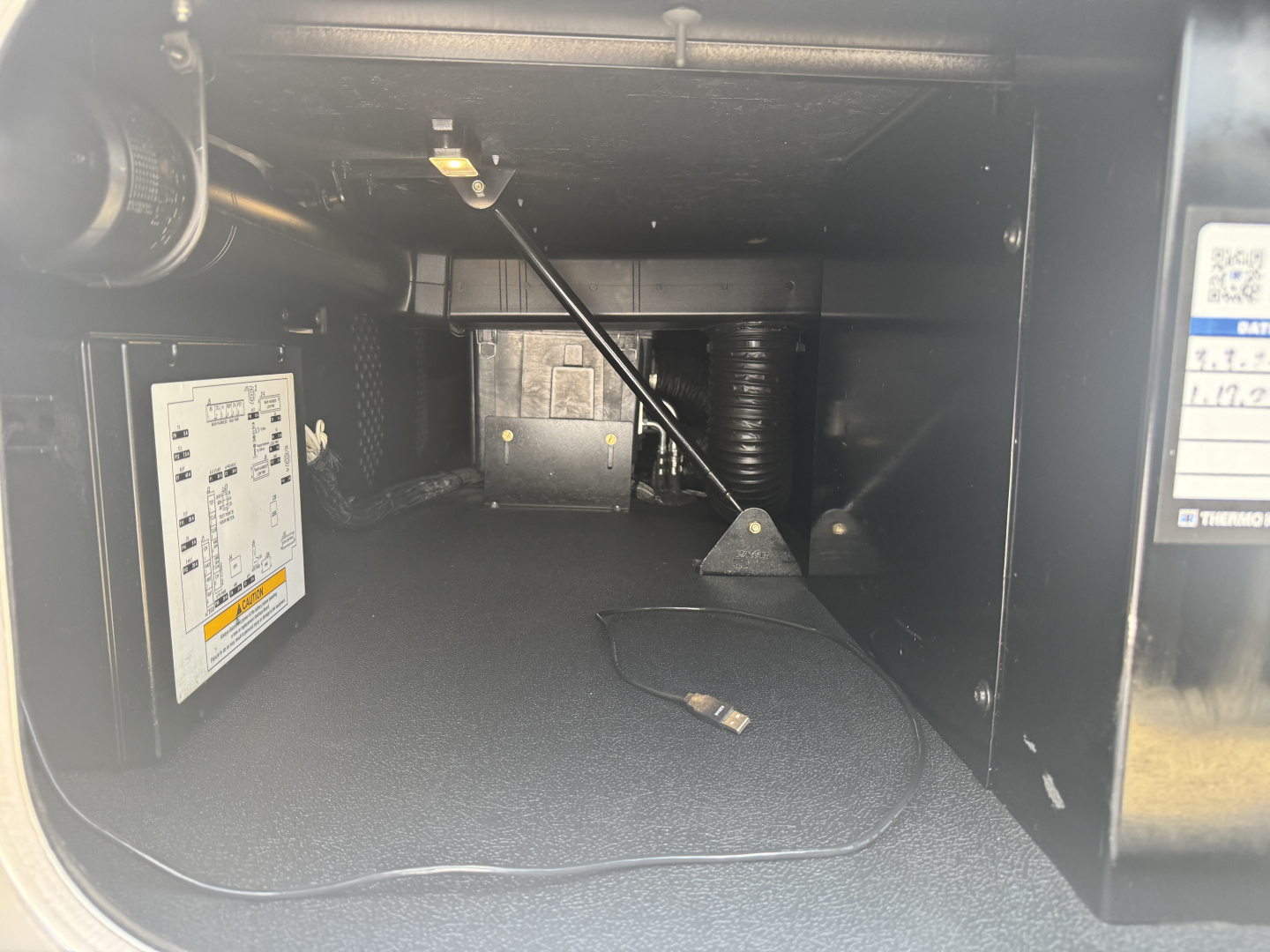 Interior of Kenworth T680 sleeper cab storage area showing a small electronic control module mounted on left wall and wiring harness with a hanging connector.