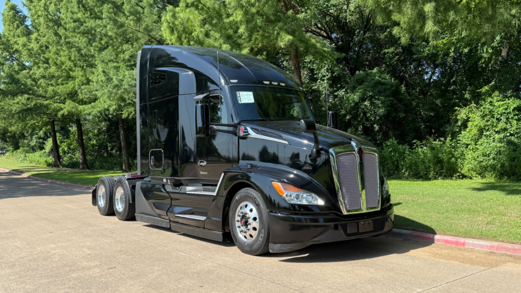 Kenworth T680 conventional sleeper tractor from front-left angle with glossy black paint and chrome grille, showing multiple axles and aerodynamic cab.
