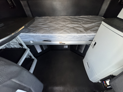 Kenworth T680 cab interior showing sleeping berth and storage area with mattress, storage bins, and a small refrigerator or cabinet on the passenger side.