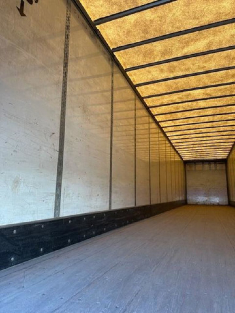 Trailer interior showing long empty cargo space with ribbed walls and overhead translucent ceiling. No equipment labels visible.