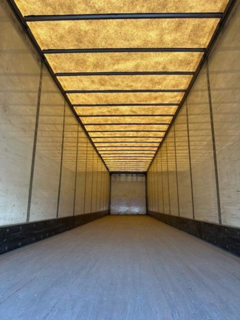Truck trailer interior showing empty cargo area with white walls, wooden roof planks, and metal framing.