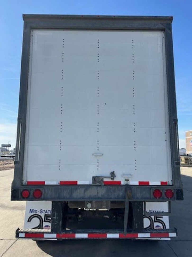 Rear view of a Wabash van trailer showing a white interior rear door with small ventilation holes, red and white reflective tape, taillights, bumper, and license plate brackets.