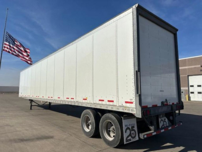 Trailer side and rear of a 2014 Wabash van trailer with triple axles, white exterior,American flag in background.