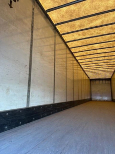 Trailer interior showing long empty cargo space with ribbed walls and overhead translucent ceiling. No equipment labels visible.