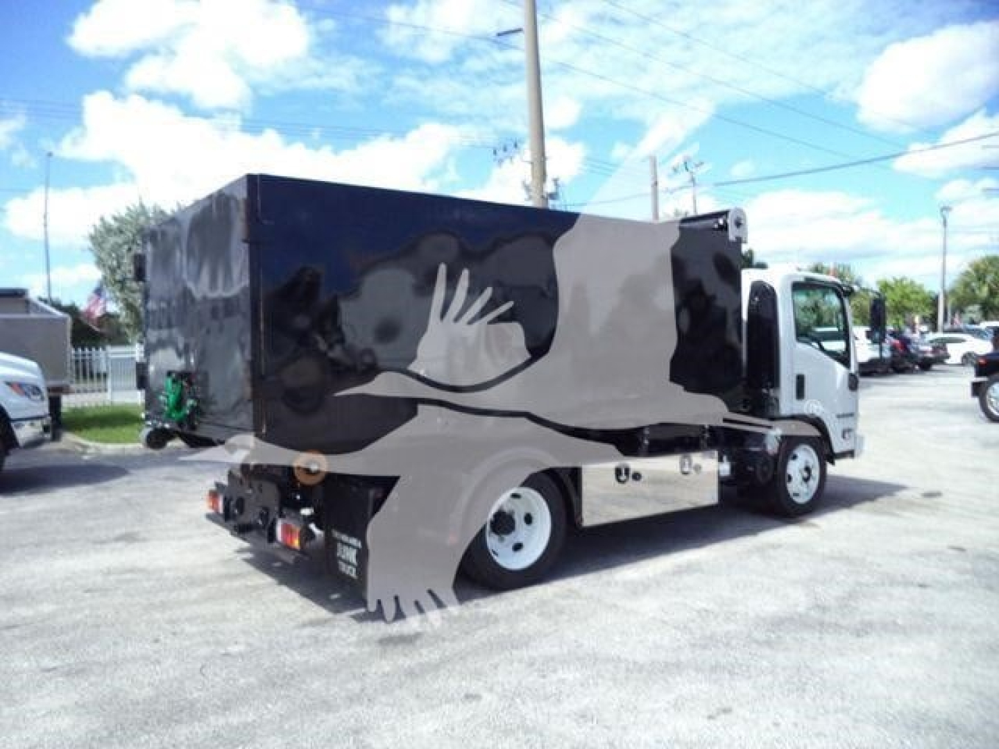 Isuzu NPR-HD hooklift truck in serviceable condition showing side and rear with black cargo box and white cab.