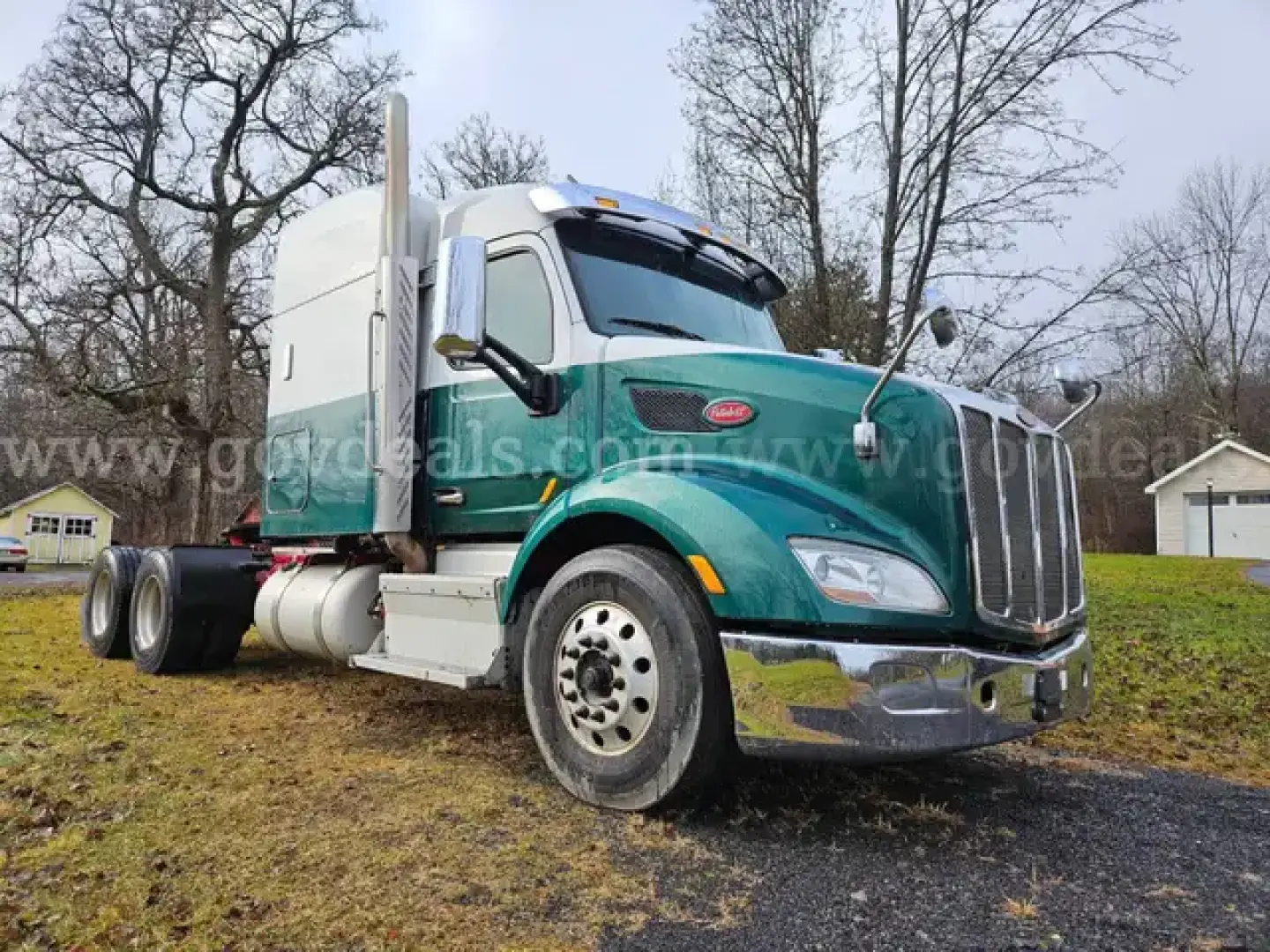 Truck exterior showing Freightliner M2 106 dump truck with teal cab and chrome bumper, side exhaust stacks, dual rear axles, and raised hood.