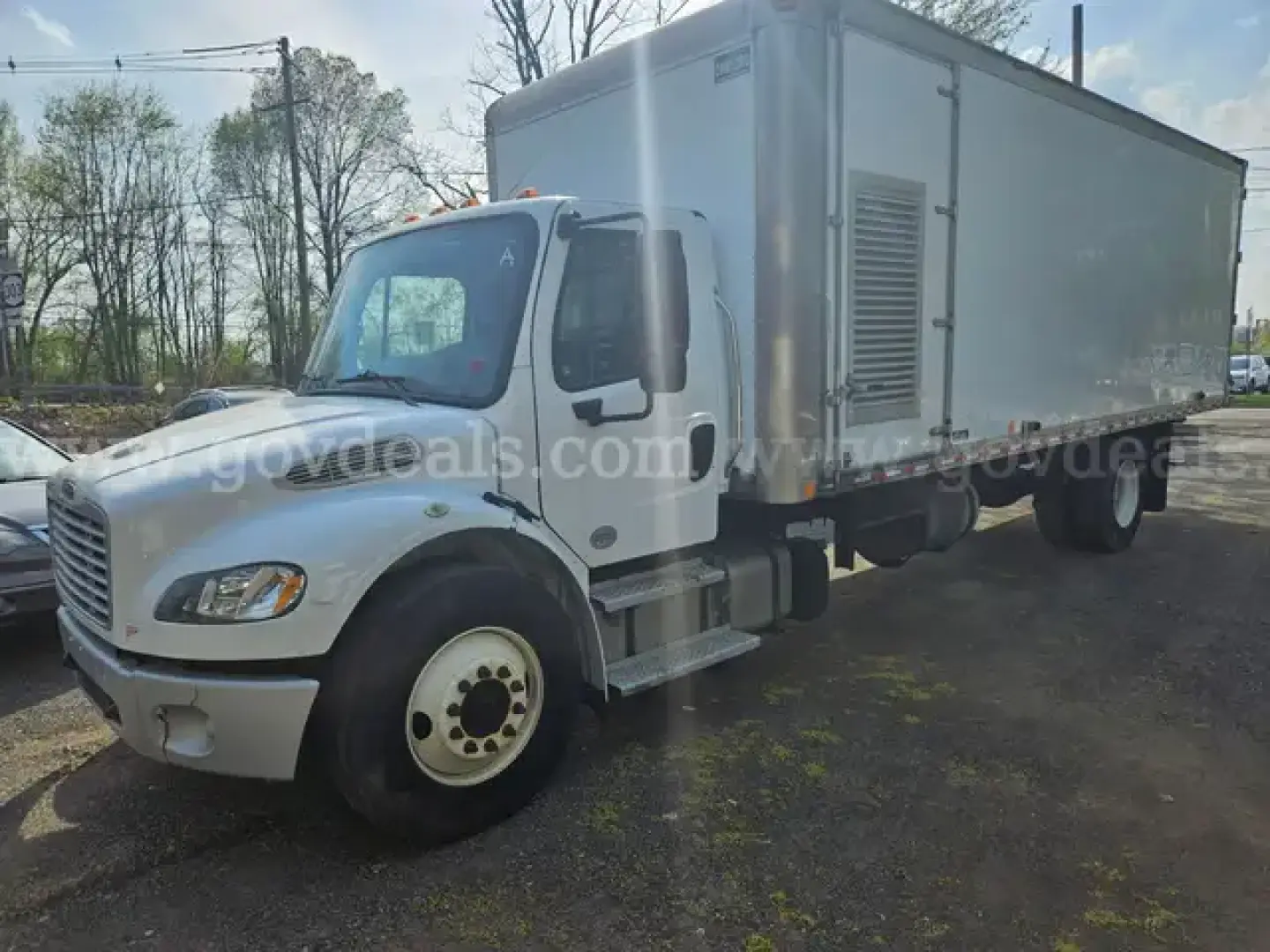 Freightliner M2 106 dump truck with light gray box and white cab, side view showing cab and cargo box.