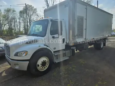 Freightliner M2 106 dump truck with light gray box and white cab, side view showing cab and cargo box.