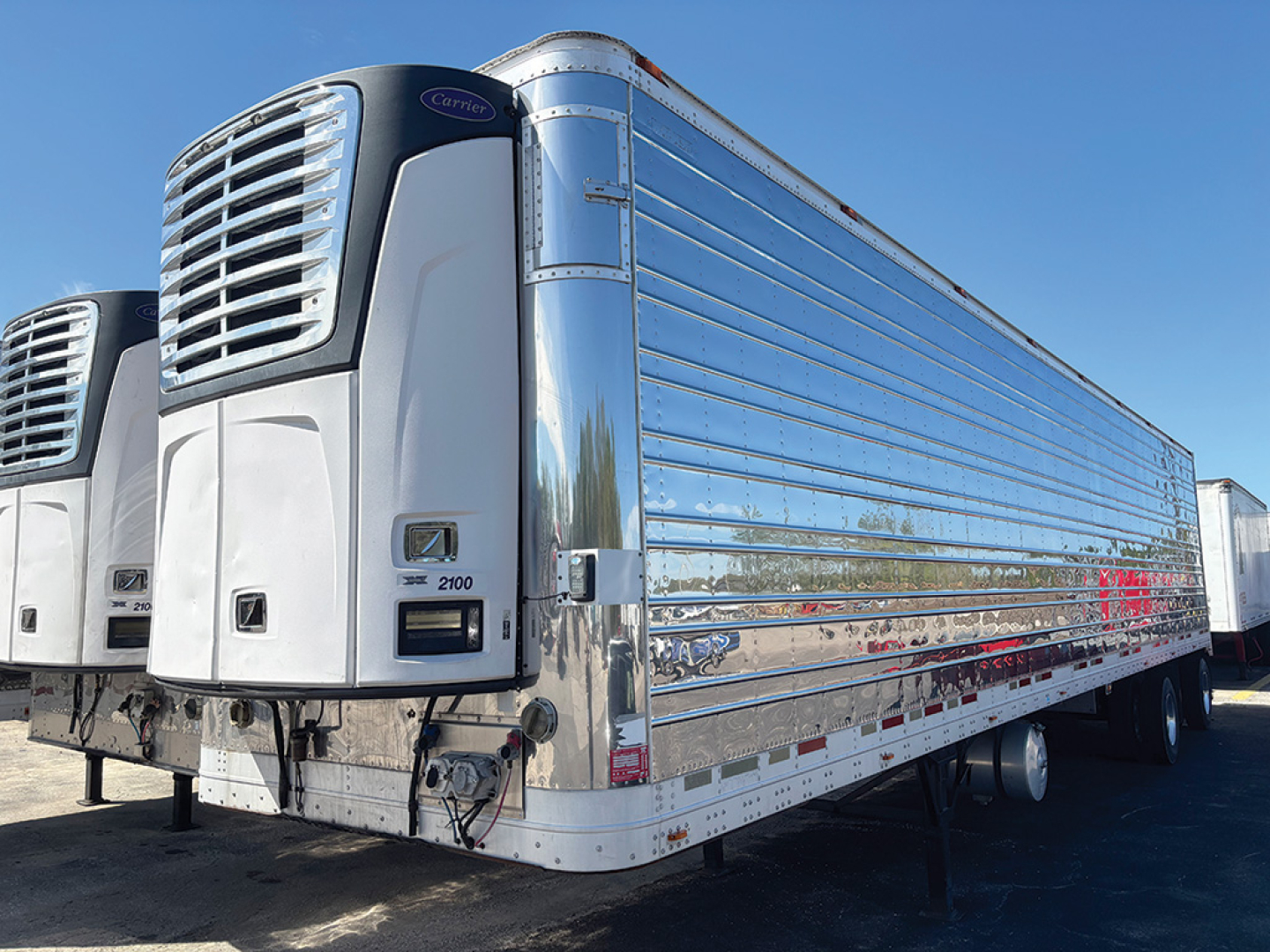 Reefer trailer front-left view showing Carrier refrigeration units and chrome stainless steel sides.