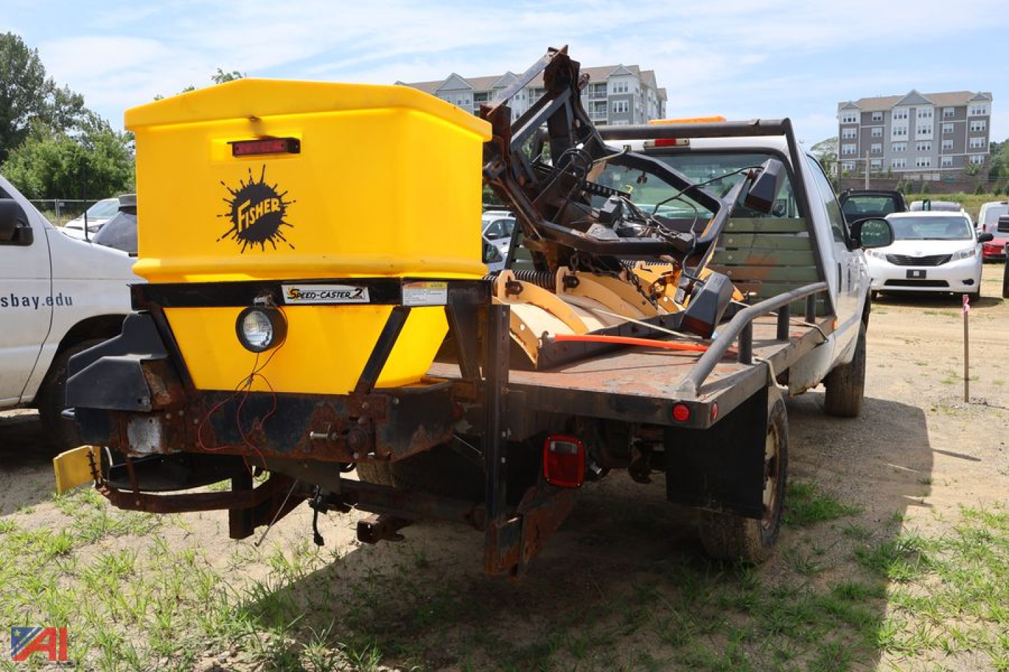 Ford F-250 Super Duty pickup with a yellow Fisher snow plow/salter attachment on a trailer hitch, rear view.