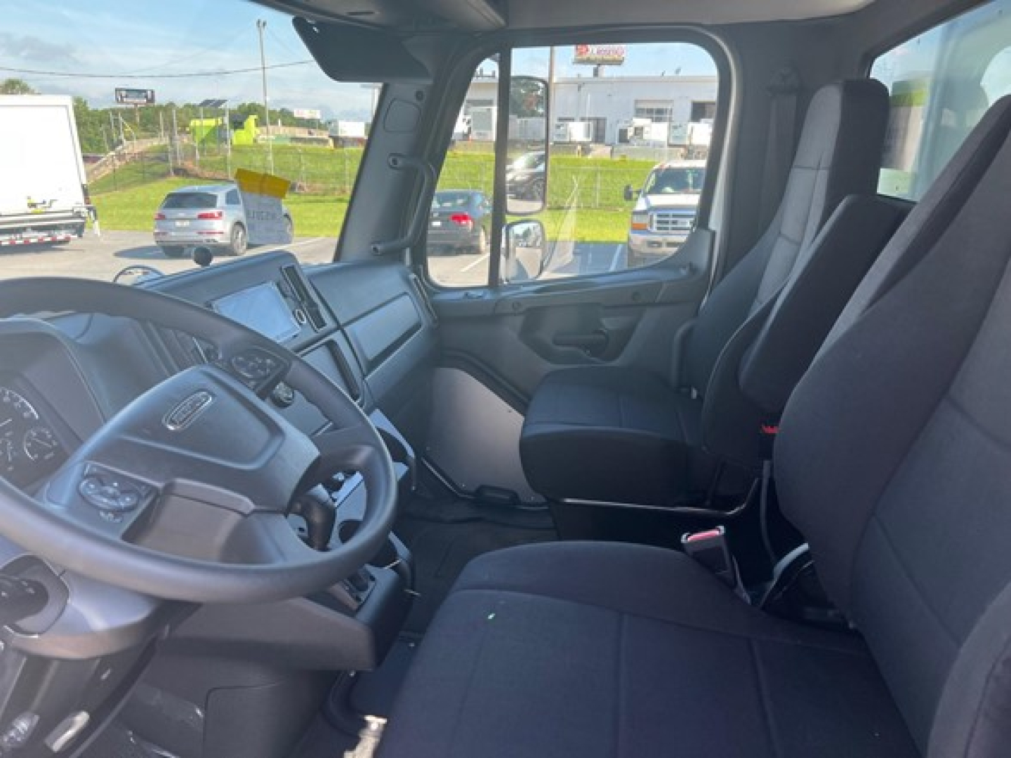 Truck cab interior showing steering wheel, dashboard, driver and passenger seats in a Freightliner Business Class M2 106 Plus cab.