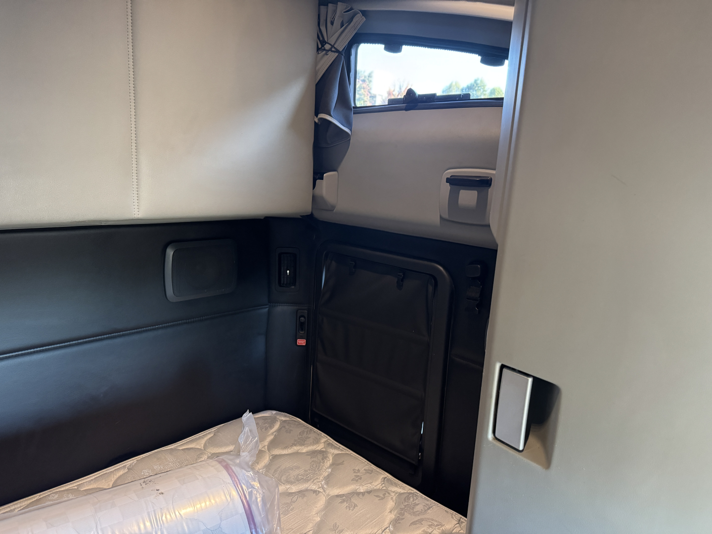 Kennworth T680 sleeper cab interior showing side wall storage and window; visible upholstery and paneling.