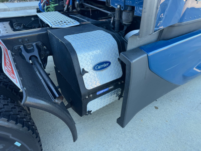 Kenworth T680 side view showing Carrier auxiliary power unit with diamond plate housing and blue truck fender.