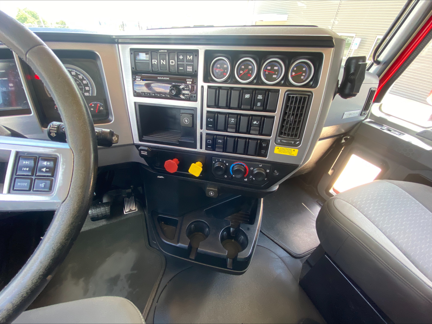 Mack AN64T truck cab interior showing dashboard controls and gauges with gear selector, warning lights, and cup holders.