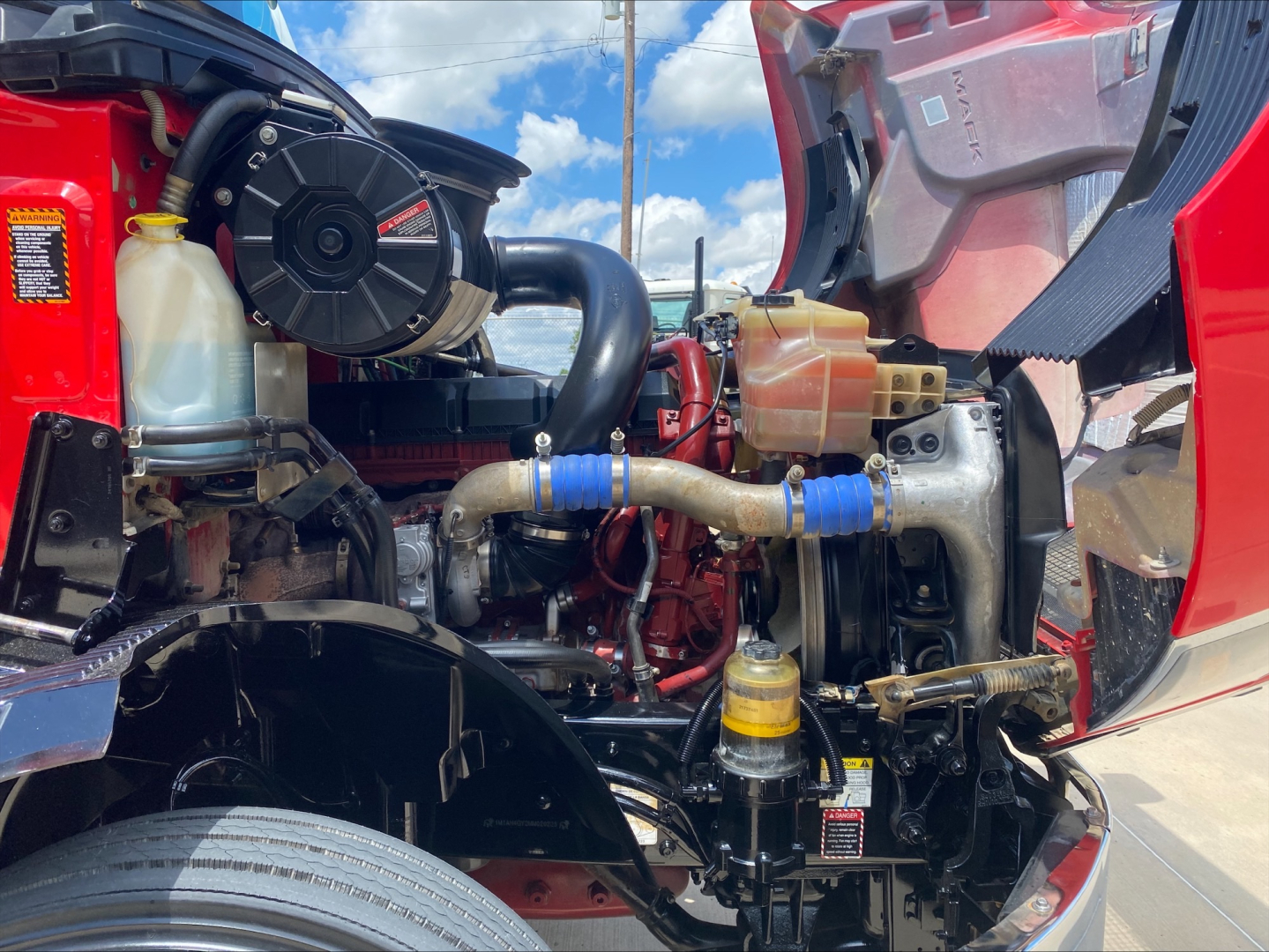 Mack AN64T engine bay showing coolant reservoir, air intake, turbo hoses, intercooler, and various hydraulic lines.