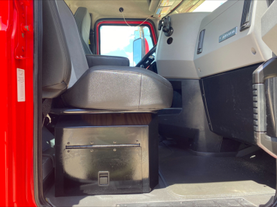 Cab interior of 2021 Mack AN64T with captain seat, dash, and storage box under seat. View shows driver footwell and entry, with red exterior visible.