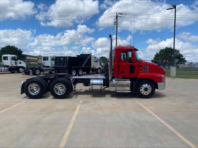 Mack AN64T conventional daycab tractor in red with three-axle rear, side view showing chassis and fuel tanks.