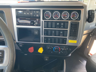 Dashboard of a Mack AN64T truck showing gauges, gear selector, switches, climate controls, and radio. Visible labels include Mack branding on the stereo panel and multiple circular gauges.