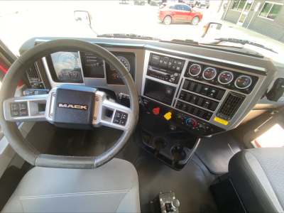Dashboard and steering wheel of a Mack AN64T truck cab showing instrument cluster, control panels, gear shifter area, and cup holders.