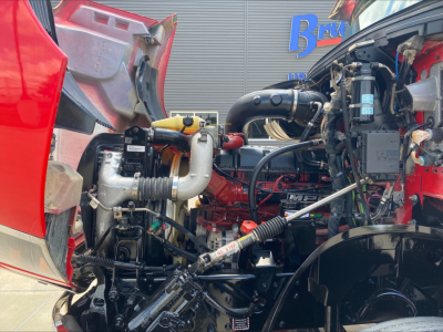 Mack AN64T truck engine bay showing red cab and various hoses, tubes, and components in view.