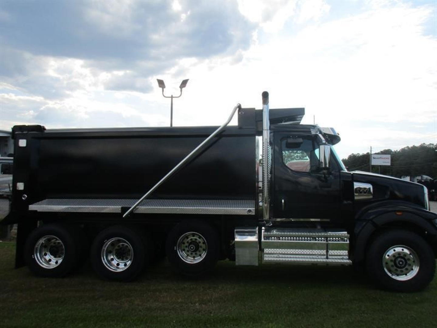 Dump truck side view showing black dump body, chrome steps, and twin rear axles on a Western Star 49X chassis.
