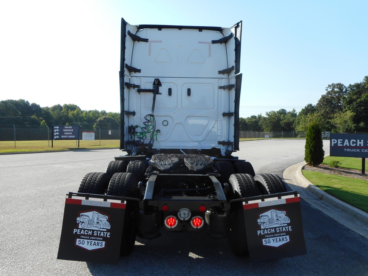 Rear view of a Freightliner Cascadia tractor with fifth wheel and dual rear axles, mud flaps showing 'Peach State 50 Years' logos, and red taillights.