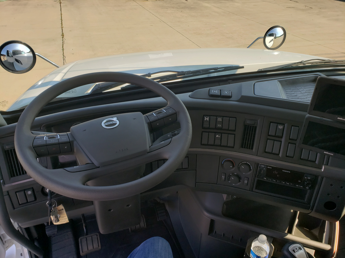 Volvo truck interior dashboard and steering wheel with steering column controls and instrument cluster; includes windshield, mirrors, and gear shifter area.