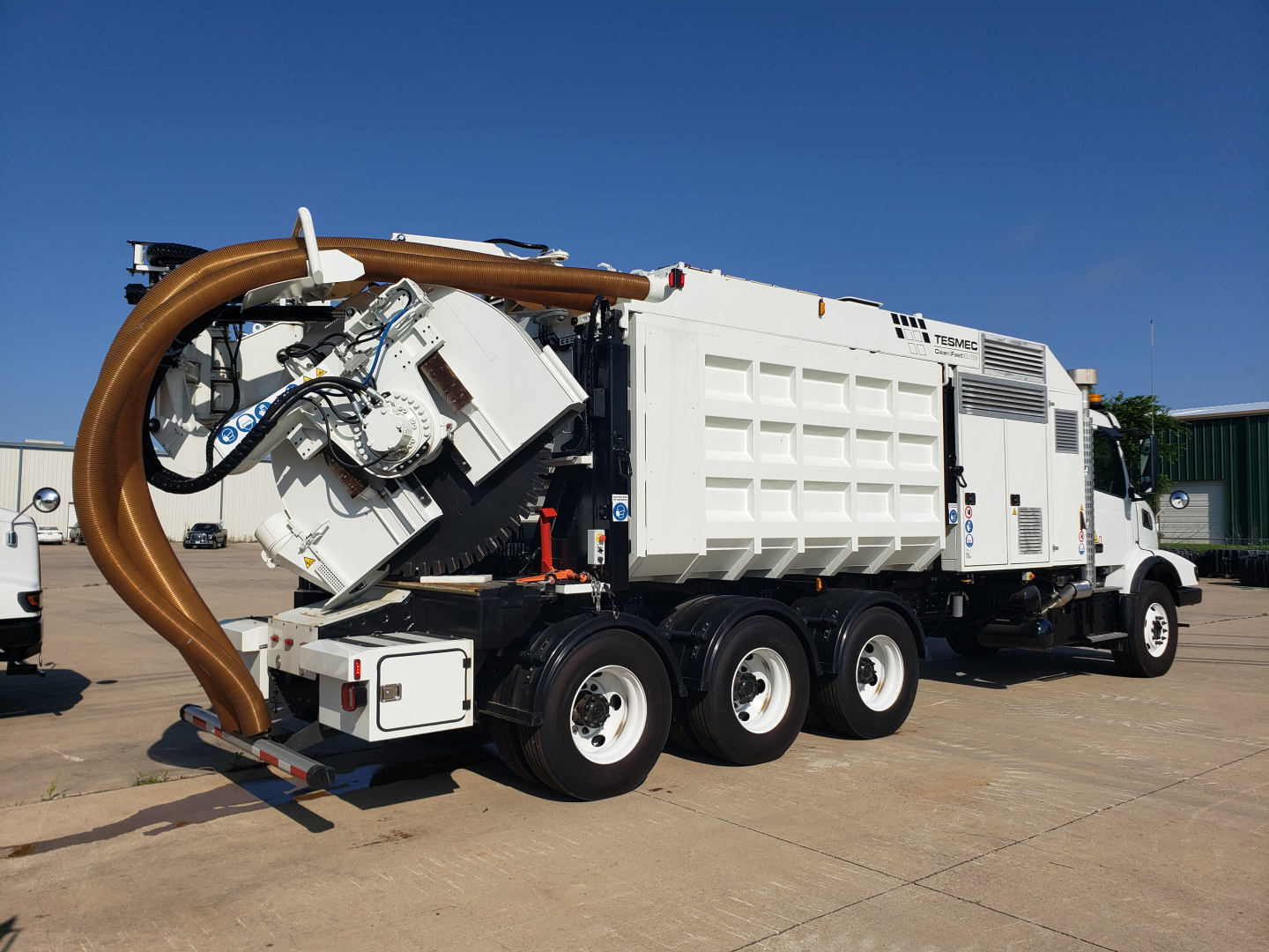 Volvo trenching truck in service bay showing large orange intake hose and white material body with multiple axles.
