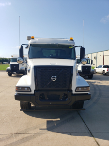 Front view of a white Volvo VHD86B300 truck showing large black grille, amber roof lights, and dual antennas.