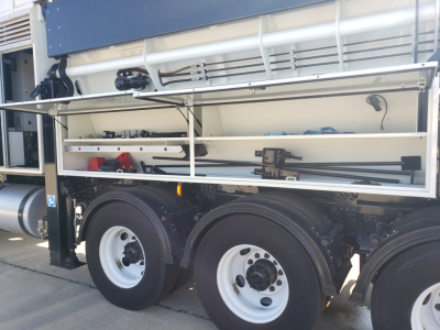 Volvo VHD86B300 truck side view showing open side compartments with tools and equipment, dual rear axles and white wheels.