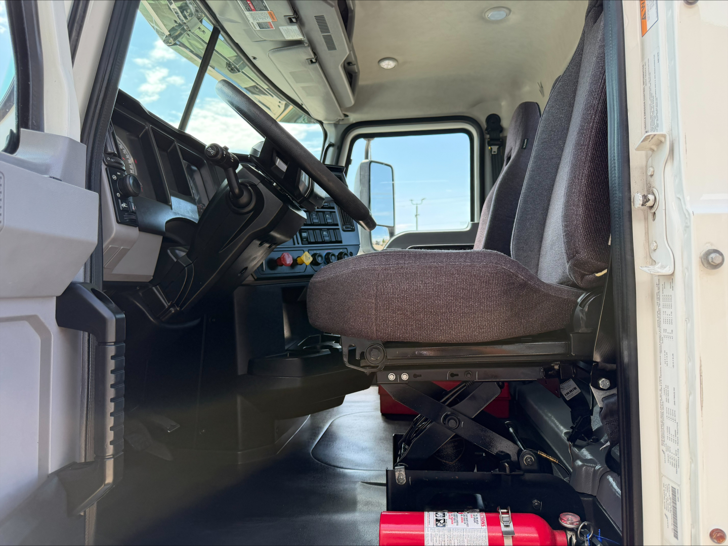 Truck cab interior of a 2020 Mack ANTHEM from the driver side, showing the dashboard, steering wheel, and driver's seat with suspension structure visible under seat.