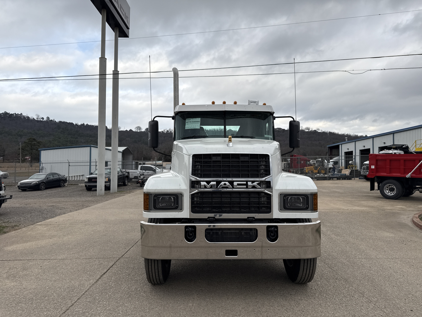 Front view of a white 2026 Mack PI64T conventional daycab truck with large grille, bumper, and dual mirrors in a dealership lot.