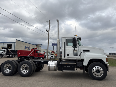 Truck side view: 2026 Mack PI64T conventional daycab with white cab, dual rear axles, fuel tank under cab, vertical exhaust stack, and chrome wheels.