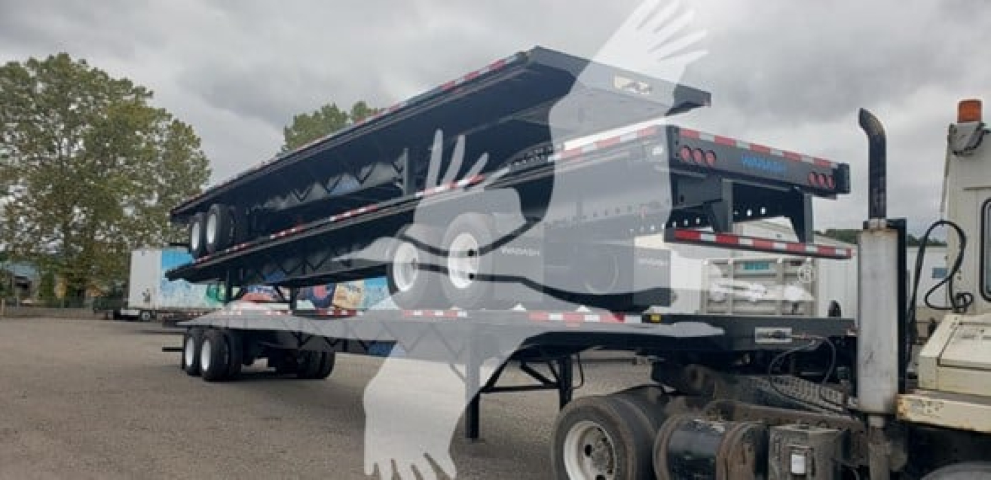 Flatbed trailer with air slider showing Wabash branding and metal frame, attached to a truck at a yard.
