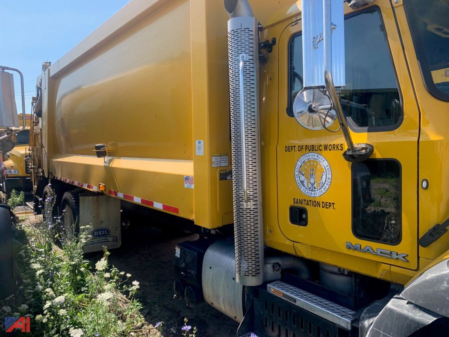 Mack garbage truck cab and dump body showing Department of Public Works emblem and side exhaust stack.