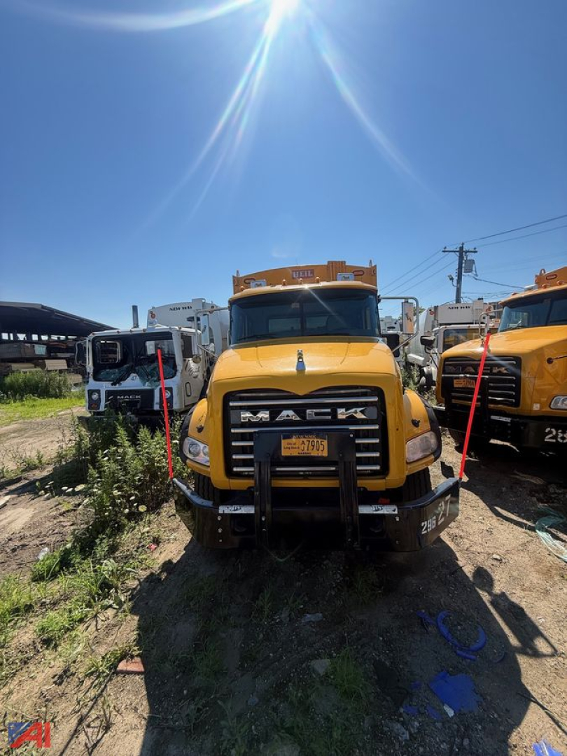 Yellow Mack garbage truck front view with bumper guards and grille, in-service equipment, other trucks in background.